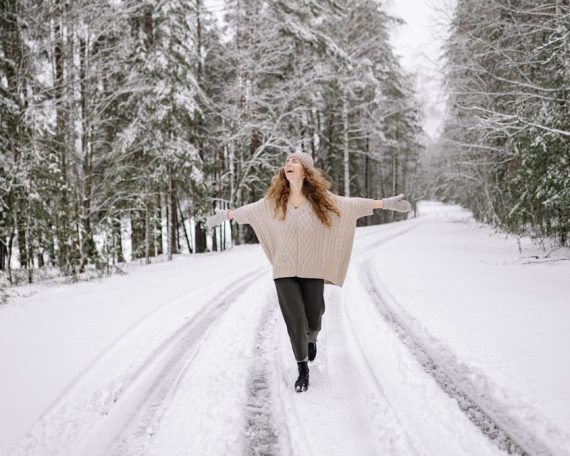 A cheerful woman with curly hair walks joyfully on a snow-covered forest road in winter.